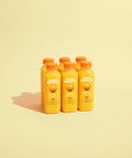 Six small square bottles filled with bright orange juice, arranged in two rows on a pale cream background with a soft shadow.